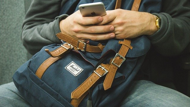 Man Looking At Smartphone On Backpack