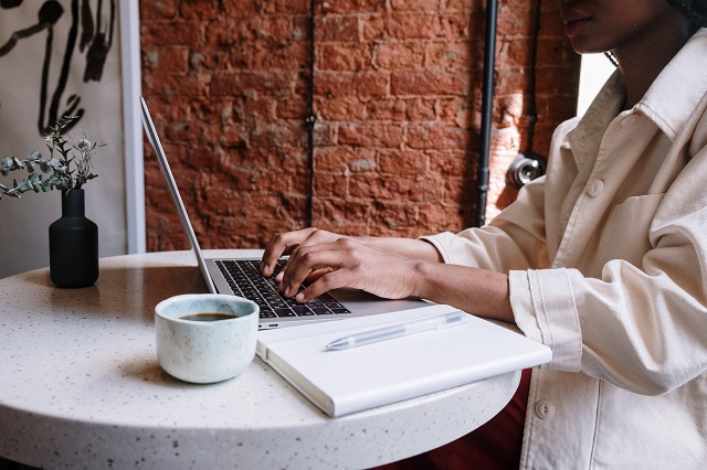 Woman typing on laptop with coffee and notepad nearby