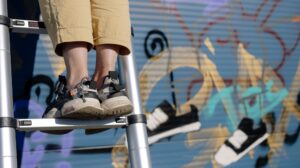 Person standing on step ladder in front of painted mural