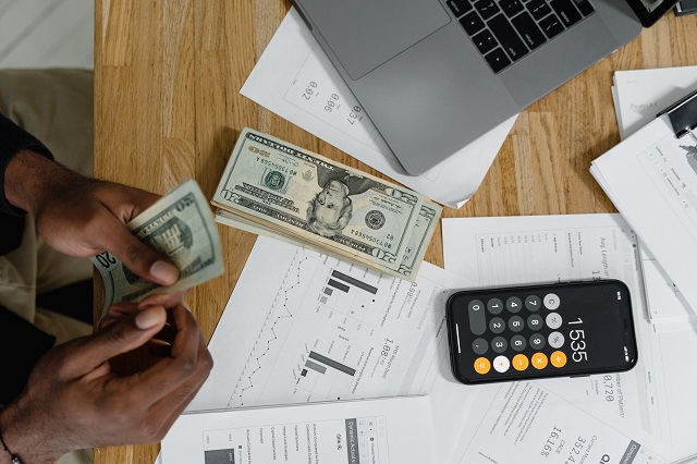 Person counting money on desk with calculator