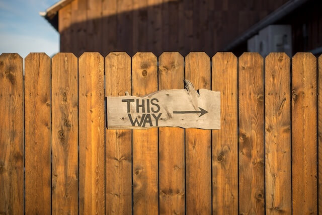 Wooden fence with sign that reads this way next to arrow pointing to the right