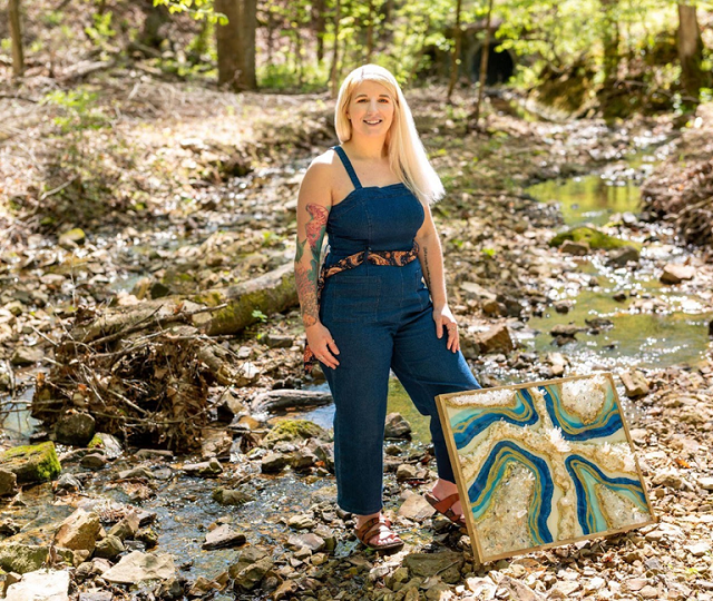 Julie Knotts standing in front of a winding creek with a geode art piece leaning on her leg