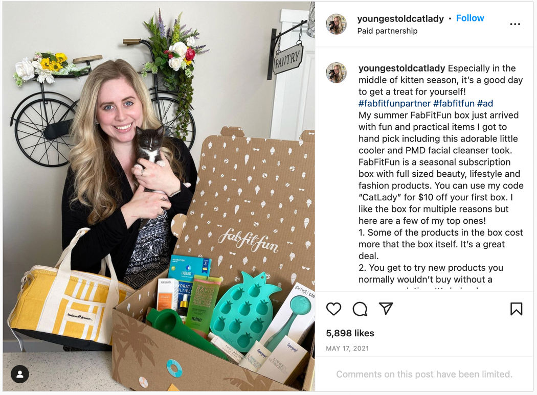 A woman holds her cat next to a FabFitFun box, the caption includes a hashtag sharing that she is a partner of FabFitFun