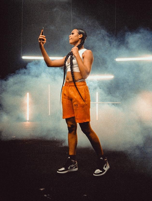 A woman in orange shorts taking a selfie with a smokey background