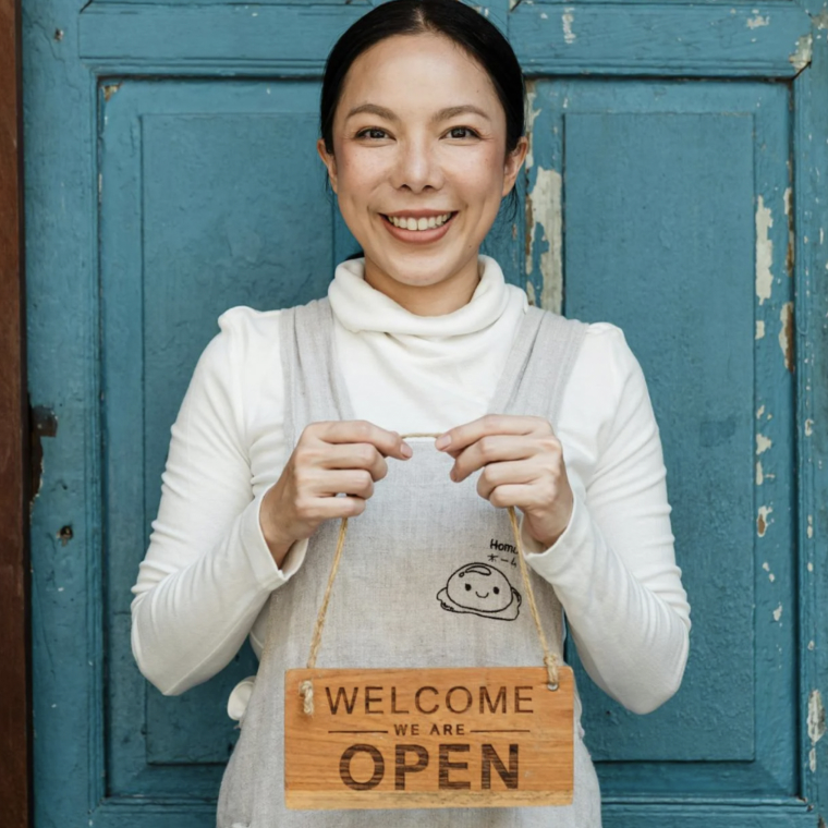 Smiling woman holding wooden “Welcome We Are Open” sign