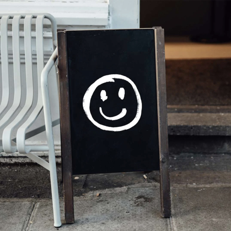 Black sidewalk sign with white smiley face outside shop