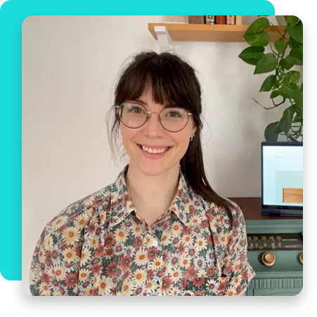 Smiling woman in floral shirt with glasses sitting beside an open laptop