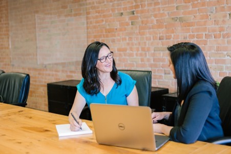 2 ladies in a work environment sitting at a table smiling in agreement