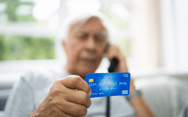 A man holding credit card and giving out its information on a phone likely in a social engineering case
