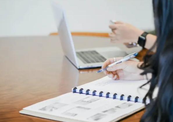 Two people reviewing a notebook and laptop on a long table
