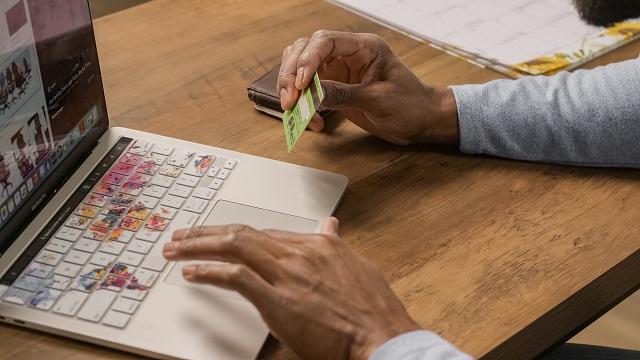 شخص يحمل بطاقة ائتمان أثناء التسوق عبر الإنترنت على جهاز كمبيوتر محمول.