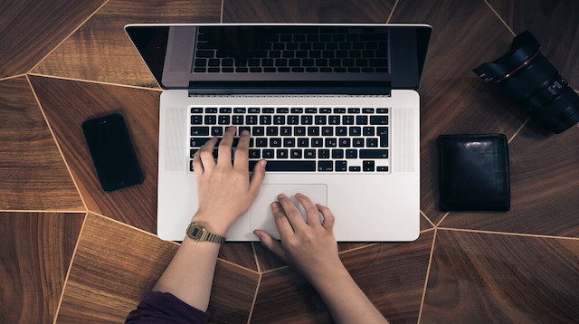 Two hands over a laptop on top of brown table