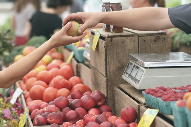 Fruit Seller Handing an Apple to a Buyer