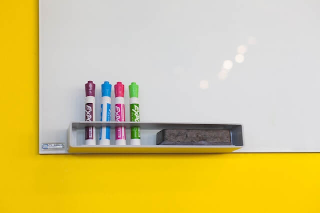 Whiteboard with markers and eraser on yellow wall