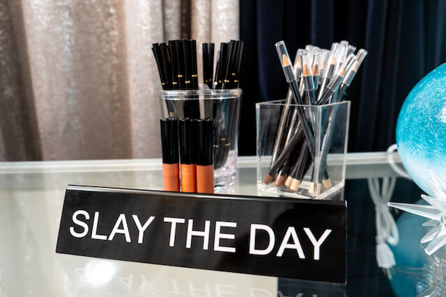 Sign reading “Slay the Day” sitting in front of makeup products