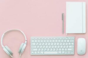Headphones keyboard mouse and planner on pink desk