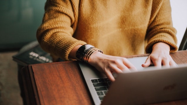 Person in yellow sweat typing on laptop at desk