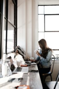 Woman sitting at desk sipping coffee and working on laptop