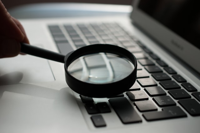 Hand holding a magnifying glass over a computer keyboard