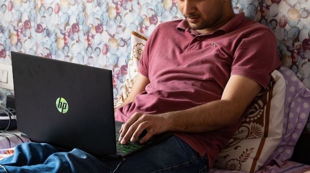 Man Working Remotely on a Laptop in Bed