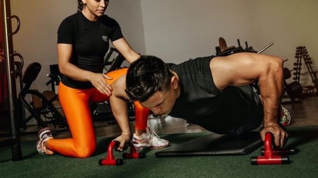 personal trainer kneeling next to male doing pushups