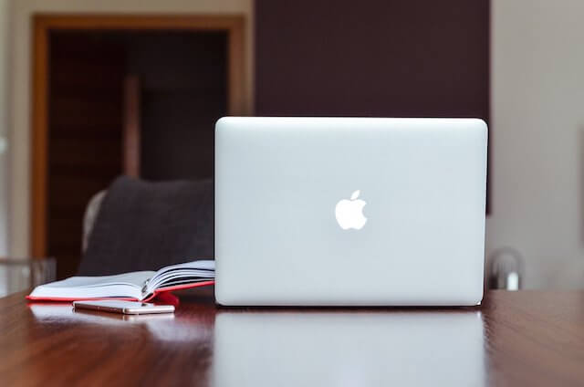 Apple laptop sitting on desk next to notebook