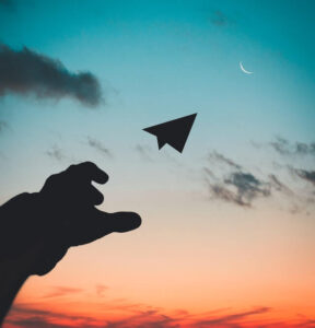 Silhouette of person throwing paper plane into sky