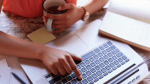 Woman Holding Coffee Cup And Typing On Laptop