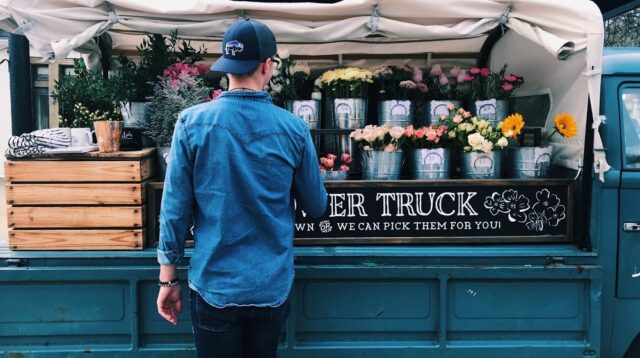 Man looking at floral display on the back of a blue truck