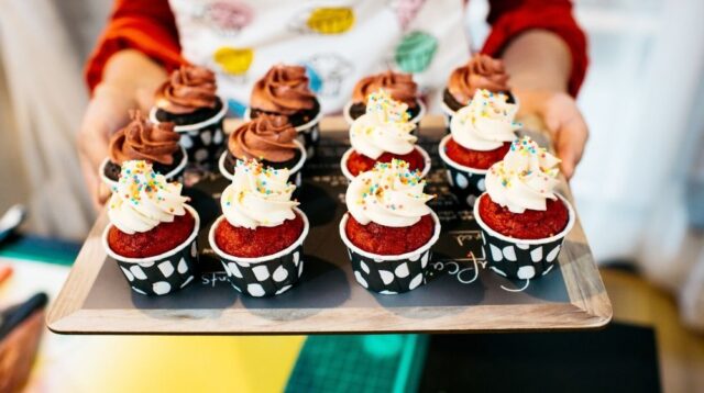 Person holding a tray of decorated cupcakes