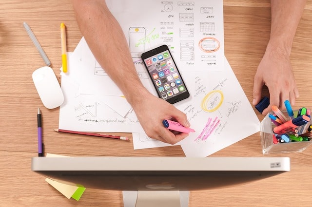 Person with design plans on desk with cell phone