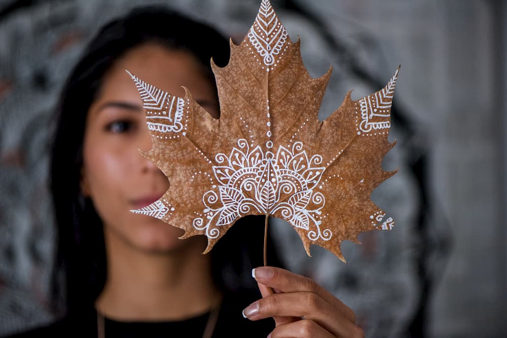 Imagen de Marcela, de Moondala, enseñando una hoja seca pintada con sus creaciones