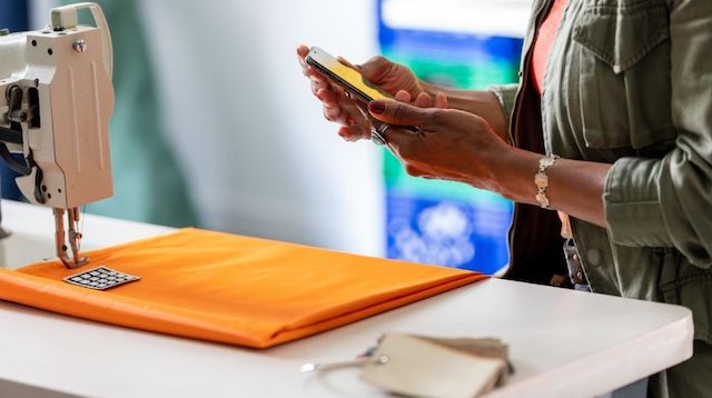 Woman Standing Near a Sewing Machine Looking at Her Phone