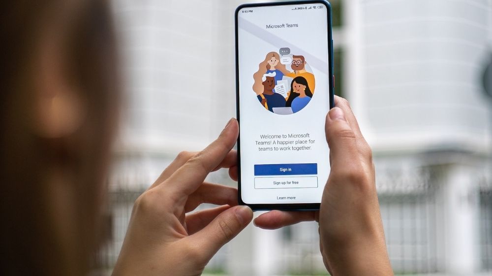 Person holding smartphone with Teams sign-in screen on it