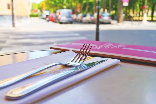 Close-up of dining utensils next to menu on table with street level views in background