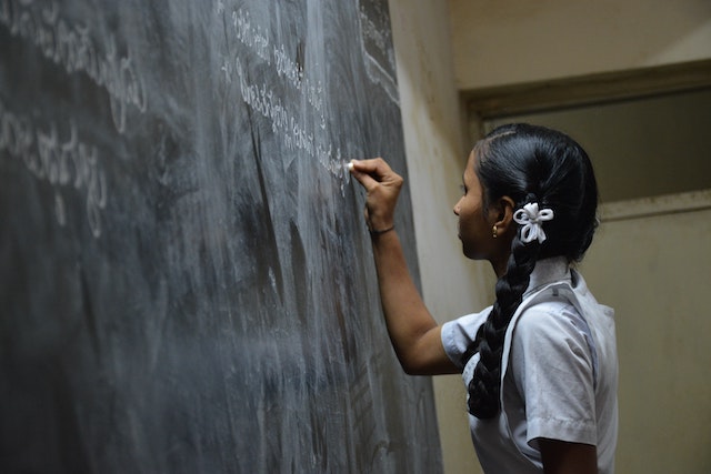 A girl in uniform writing on the blackboard