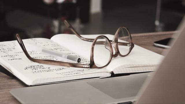 Glasses sitting on a notebook near a laptop