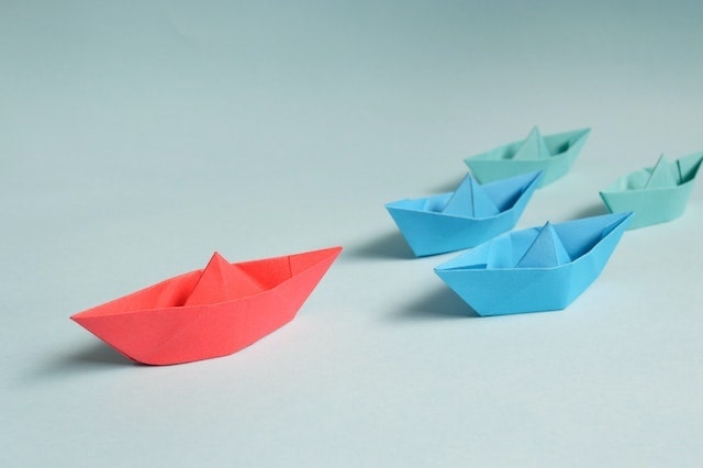 Large red paper boat leading group of smaller blue boats