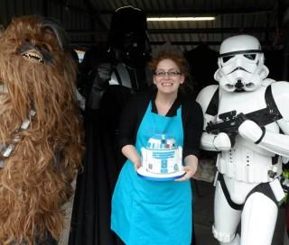 Baker Natalie Porter holding a Star Wars-themed cake, flanked by a Storm Trooper and wookie