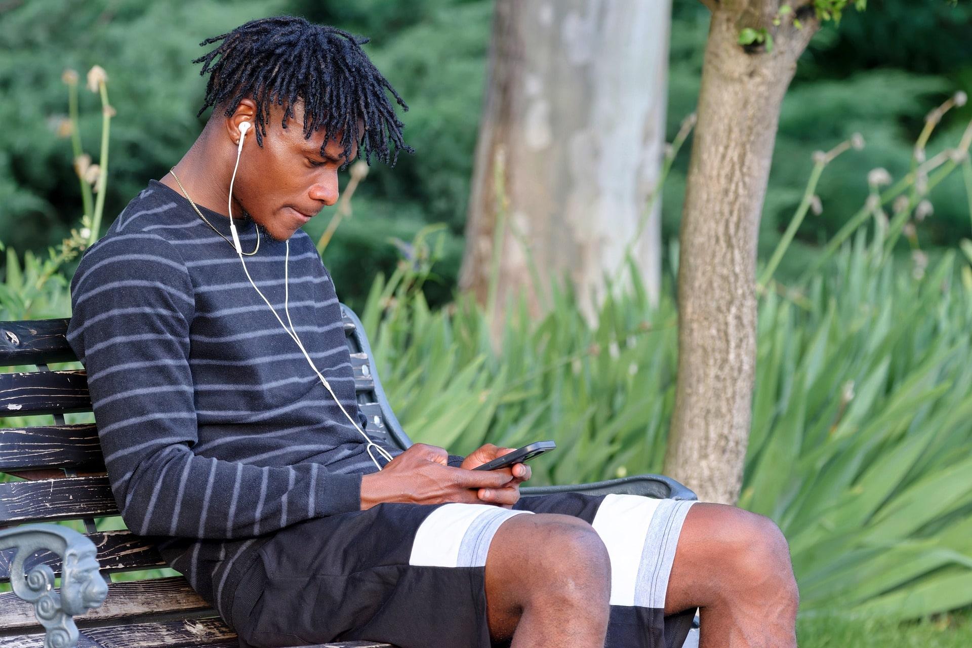 Man sitting on a park bench listening to a podcast