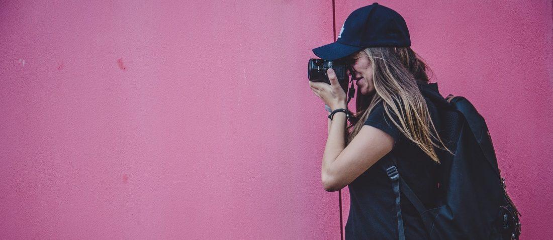 Woman taking a photograph next to a pink wall