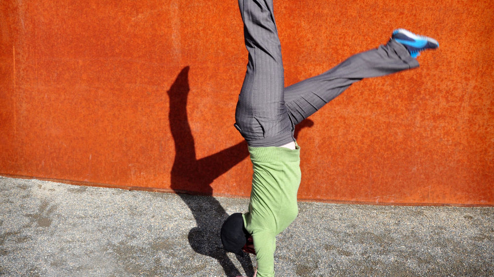 person doing handstand against orange wall