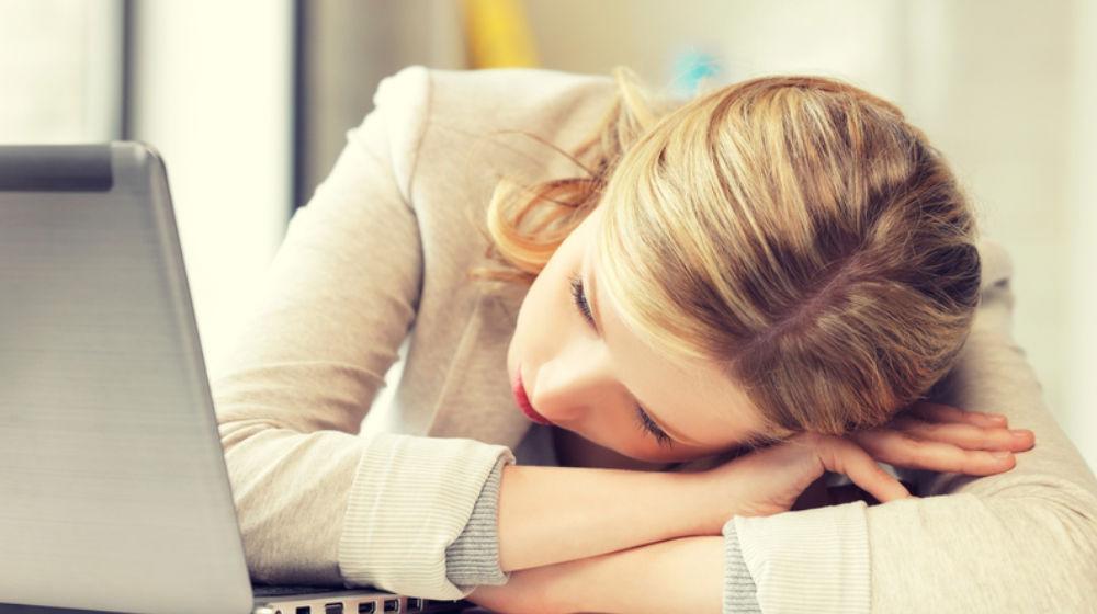 woman with head on desk to illustrate how exhausting it is to over-commit