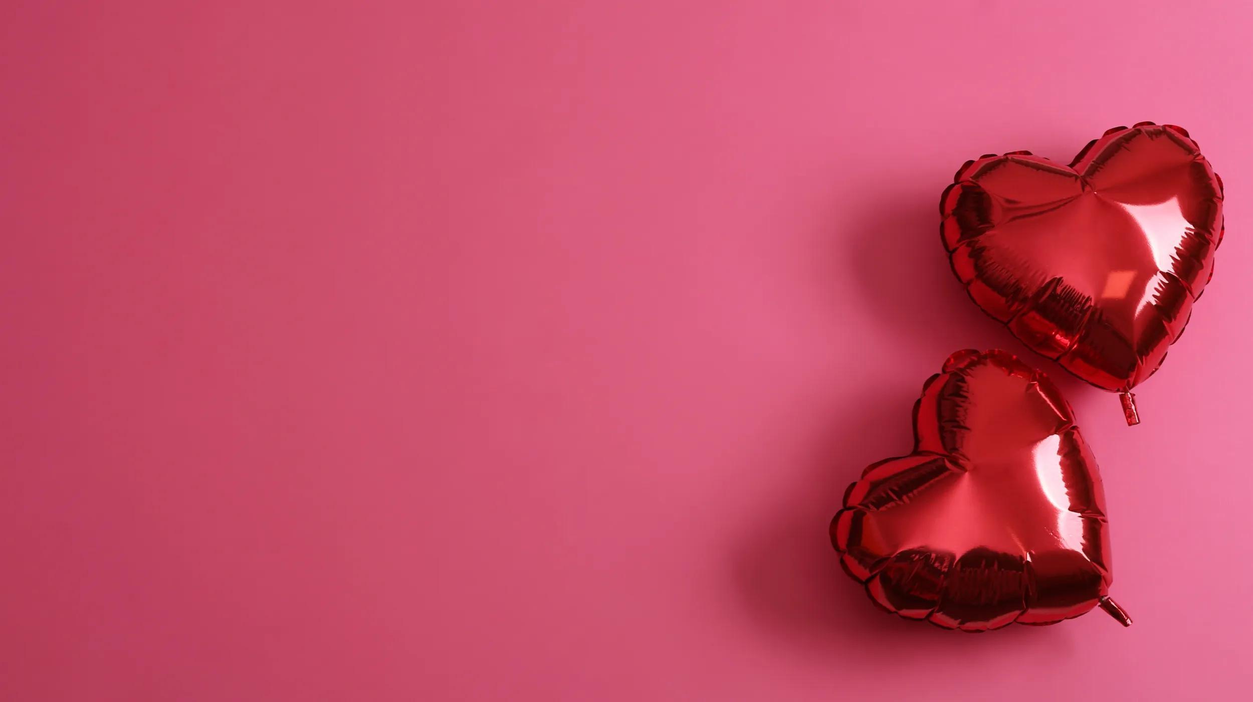 Two heart-shaped balloons on a pink background.