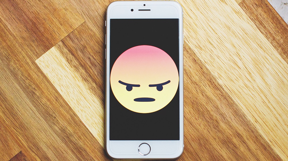 Mobile Phone With An Angry Emote Resting On Desk