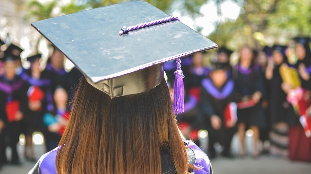 Graduate standing up at graduation ceremony in hat and robe