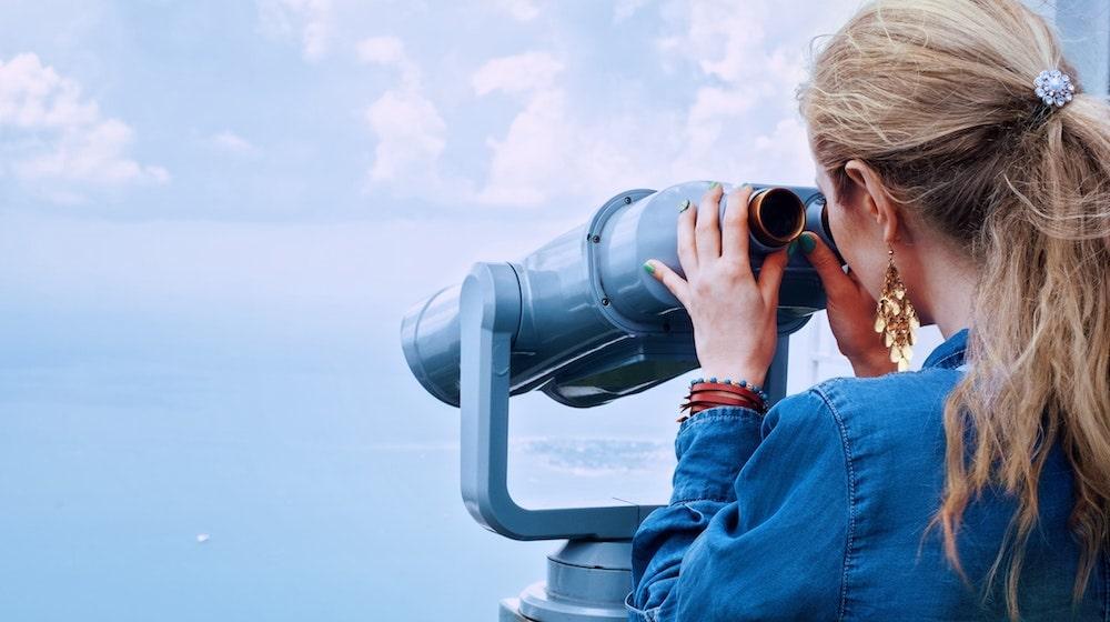 Woman looking through binoculars over coast