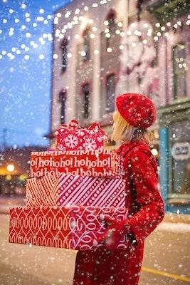 Woman on snowy street holding holiday presents
