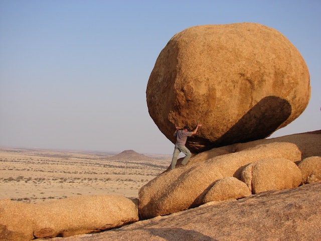 Man pushing boulder up hill