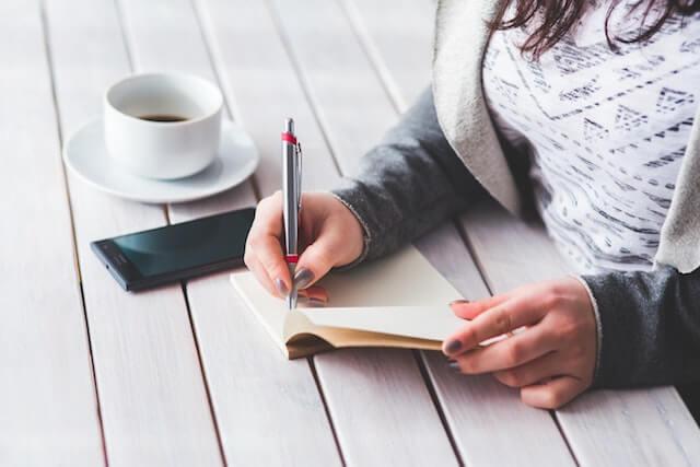 Woman writing in a journal with a cup of coffee